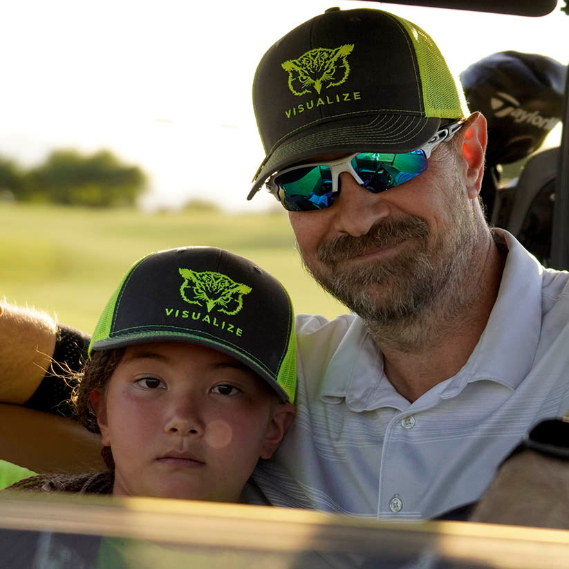 A young golfer with her dad wearing awesome yellow and gray visualize hats.